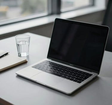 A minimalist and sophisticated office workspace in Brno, featuring a sleek laptop, a notebook, and a glass of water on a soft grey desk, with a backdrop of a modern window.