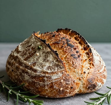 A beautifully composed close-up of an artisanal sourdough loaf and fresh herbs in a Scandinavian-style North American / US restaurant kitchen. Soft, diffused afternoon light highlighting textures of the bread and the Matte Forest Green background.