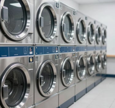 A wide shot of a commercial laundry room featuring a row of high-end, stainless steel washing machines and dryers. The lighting is bright and clean, emphasizing efficiency and professional standards. Accents of #3B607D in the shadows and machinery highlights.