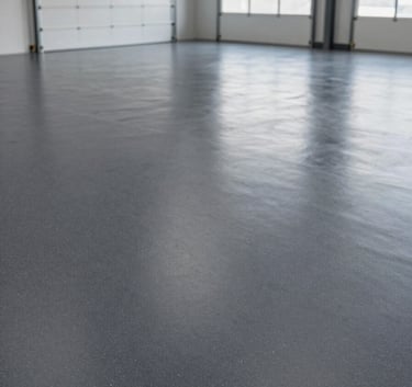 An expansive industrial garage with a professional, dark gray epoxy floor featuring light gray decorative flakes. The space is organized and clean, emphasizing the durable and easy-to-clean nature of the flooring under bright, even lighting.