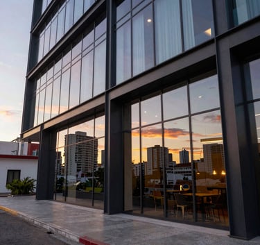 Exterior wide shot of a contemporary luxury hotel with large glass windows and steel structures, reflecting a sunset in a vibrant Latin American city.