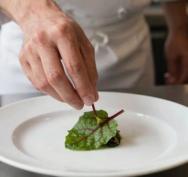 High-resolution shot of a chef's hand carefully placing a tiny red-veined sorrel leaf on a white plate, soft-focus background, elegant lighting, North American luxury restaurant kitchen.