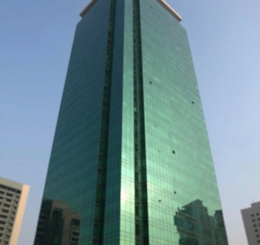 A professional low-angle shot of a modern commercial high-rise building in Karachi's financial district, reflecting a clear blue sky. The composition is sleek and modern, incorporating deep greens like #1A322C in the building's glass reflections and shadows.