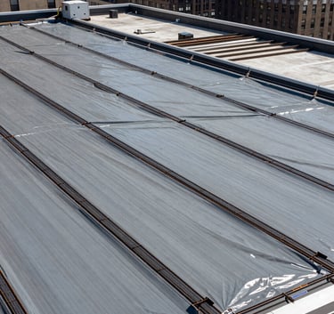 A vast commercial rooftop in New York City with newly installed gray waterproof membranes and structural steel reinforcements, wide angle, bright daylight, North American / US (New York City).