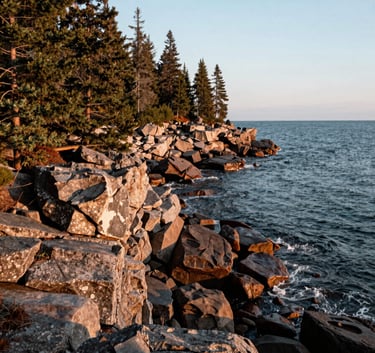 A wide-angle landscape photograph of the rugged Upper Peninsula coastline along Lake Superior. Jagged rocks and evergreen trees under a crisp morning sky, North American Great Lakes region, high-resolution and authentic feel.