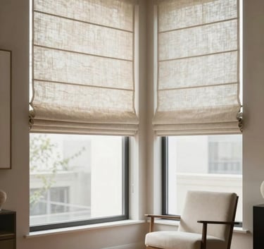 A beautiful window corner featuring high-end Roman shades in a neutral linen. The room is styled as a luxury showroom with polished wood floors and a single designer chair, exuding a high-end interior design brand atmosphere.