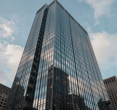 An architectural low-angle shot of a glass-and-steel skyscraper in a North American / US financial district, reflecting a soft blue sky and light gray clouds, conveying stability and professionalism.