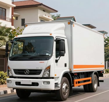 A high-end, clean white and orange logistics truck parked on a wide street in a modern South Asian / Indian residential area during bright daylight. The vehicle looks well-maintained and professional.
