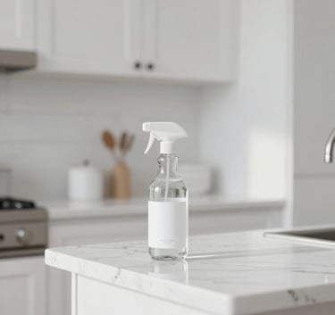 A minimalist white kitchen setting with a focus on a marble countertop and a glass bottle of cleaning spray. Bright and airy lighting, North American / US interior design, emphasizing clean lines and white space.
