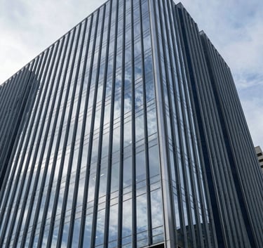 A low-angle shot of a sleek, glass-fronted corporate headquarters reflecting a pale silver sky, with sharp architectural lines in steel blue and dark navy.