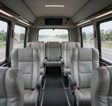 Interior view of a luxury motorcoach with spacious light gray leather seats and large windows overlooking a North American highway.