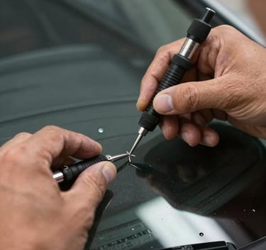 A close-up photograph of a technician's hands using professional tools to carefully repair a small chip on a windshield, focusing on precision and safety in a North American setting.