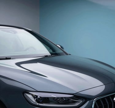 A sleek, dark high-performance vehicle parked in a professional detailing studio. The hood reflects the overhead soft-box lighting with mirror-like clarity. The environment is clean and modern, incorporating brand colors #001220 and #6D97AD in the studio accents. Meticulous craftsmanship atmosphere.