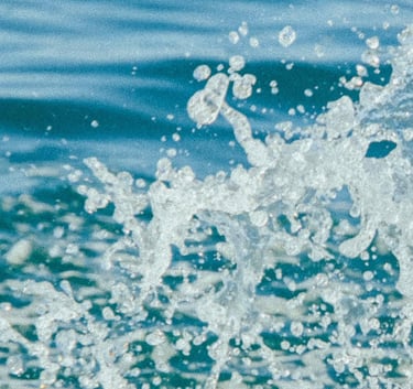 A close-up of dynamic ocean water splashing with white foam and droplets against deep blue waves.