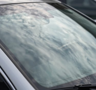 Close-up photography of a pristine vehicle windshield with a clear reflection of the sky, highlighting the smooth finish and high quality of the glass in a professional North American automotive setting.