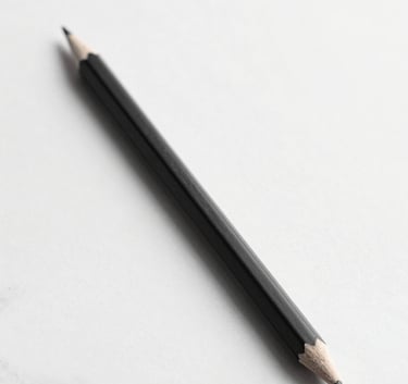 A minimalist studio shot of a single, perfectly sharpened black graphite pencil resting on a sleek white marble surface. Sharp, dramatic shadows extend from the pencil, creating a high-end, artistic feel. Monochromatic palette of #0A0A0A and #F7F7F7.