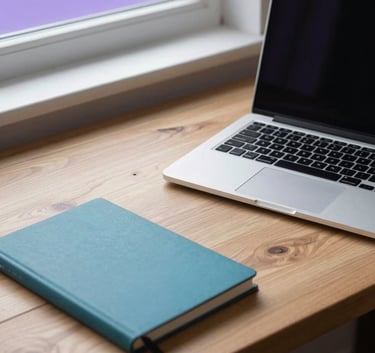A high-quality, minimalist hero image of a clean wooden workspace featuring a silver laptop and a teal notebook. Soft purple morning light streams in from a window. North American / International.