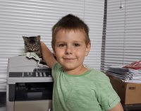 A 6-year-old smiling boy in a green T-shirt petting a tabby cat.
