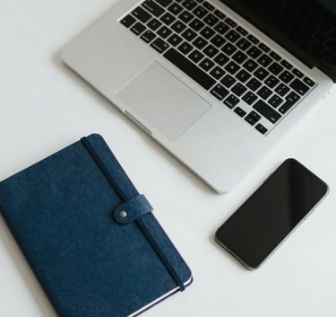 A top-down view of a clean desk with a high-end laptop, notebook, and smartphone, soft natural lighting, professional minimalist aesthetic, light gray and blue tones.