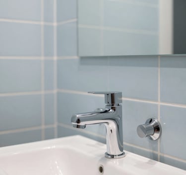 A photography of a beautifully finished modern bathroom in a Western European / French residence, showing sleek plumbing fixtures and pale sky blue tiling. The style is minimalist and clean, suggesting high-quality execution and modern design.