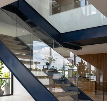 Professional architectural photography of a dark navy steel and glass staircase in a modern South American / Brazilian residential lobby, emphasizing geometric symmetry and reflections.