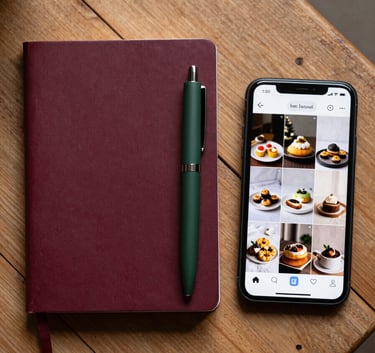 A top-down view of a rustic wooden table in a North American / European setting, featuring a deep ripe crimson notebook, a matte forest green pen, and a high-end smartphone displaying a curated social media feed of artisanal food photography.