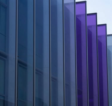 A sophisticated abstract close-up of layered glass panels catching light in gradients of indigo blue and deep violet. The composition is clean and minimalist, conveying a sense of structure and innovation in a North American architectural context.
