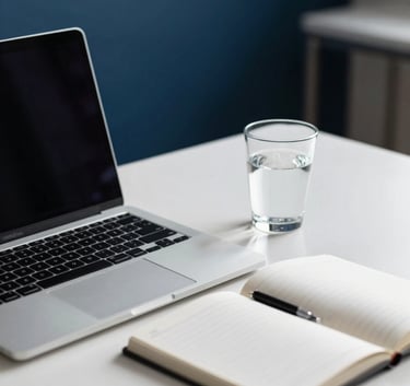 Minimalist professional desk in a French study, featuring a sleek silver laptop, a white notebook, and a glass of water, with deep blue and white tones in the blurred background.