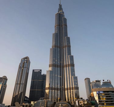 High-end luxury skyscraper in Ajman at dusk, illuminated by golden lights reflecting on its glass facade. Wide-angle architectural photography capturing the modern skyline of the Middle Eastern / Gulf region.