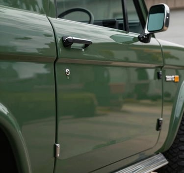 A studio photograph focusing on the chrome lettering of a classic Bronco on a dark forest green body, with soft reflections of a North American / US garage setting.