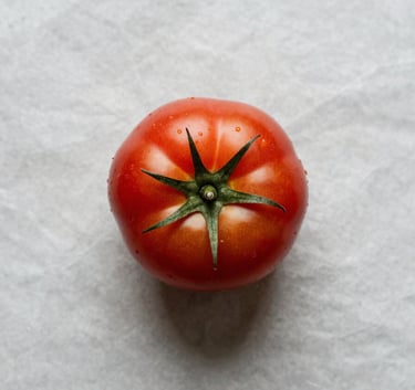Top-down professional photography of a single, perfectly ripe heirloom tomato on a Crisp Parchment background, minimalist and high-contrast editorial style.