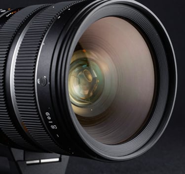 An artistic shot of a high-end anamorphic camera lens reflecting the lights of a sophisticated European studio. The lighting is dramatic and dark navy, emphasizing the precision engineering and glass quality.