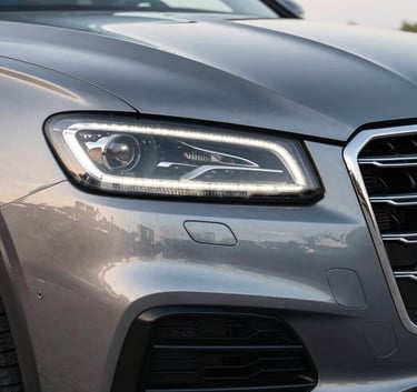A detailed shot of a luxury vehicle's front grille and sparkling clean headlight, reflecting a bright North American sky, emphasizing perfection and a premium finish in a clean professional environment.