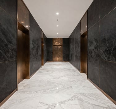 A wide-angle photography shot of a sleek, contemporary agency office in the Middle Eastern region, with white marble floors, dark charcoal walls, and bronze decorative elements.