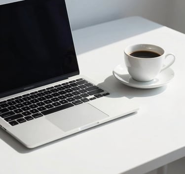 A crisp, professional photograph of a laptop and a cup of coffee on a minimalist white desk in a bright North American creative studio. The composition is clean, emphasizing a data-driven, organized workspace with soft steel blue shadows.