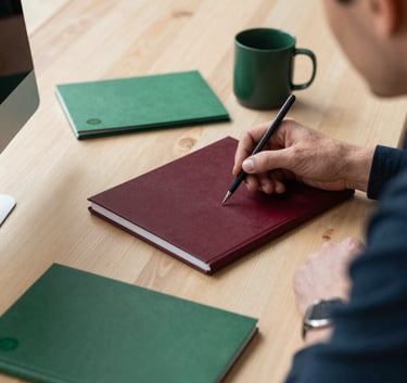 A professional in a modern Northern European / Scandinavian office setting, sitting at a desk made of light wood, planning social media content with deep ripe crimson and matte forest green stationery, bright morning light.