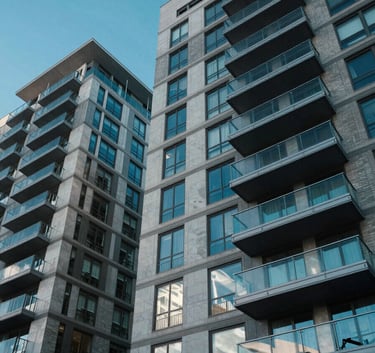 A low-angle view of a modern luxury apartment complex in Denver with glass balconies reflecting a bright electric blue sky. Professional photography, sharp focus, North American / US urban setting.