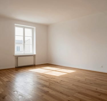 Photography of a spacious, completely empty living room with clean off-white walls and polished wooden floors in a European apartment. Sunbeams entering through a large window.