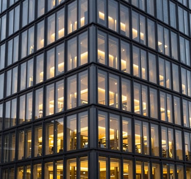 A sleek, modern office building exterior in a German city like Cologne, dusk lighting with windows glowing warm light, steel and glass architecture.