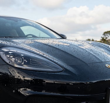 Close-up of a high-end black sports car with water beading on the hood after a professional wax, clean reflections of a bright Australian Brisbane sky, sharp focus, masculine and premium aesthetic.