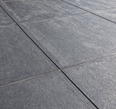 Wide-angle photograph of a premium stamped concrete driveway in a North American / US suburban home. The texture is a deep slate grey with silver highlights, looking clean and durable under bright daylight.