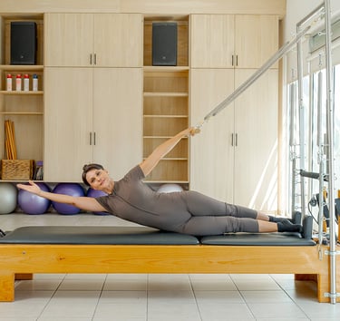 Woman performing a side-lying torso stretch using the springs of a Cadillac Pilates unit.