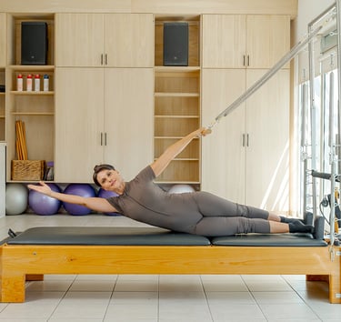 Woman performing a side-lying torso stretch using the springs of a Cadillac Pilates unit.