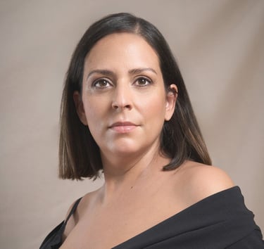 Professional headshot of a woman with dark hair wearing a black off-the-shoulder top.