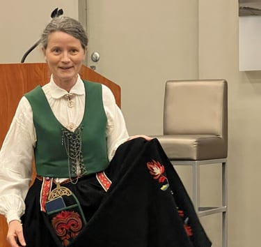 A woman in a bunad with a green vest holding the apron to show detail