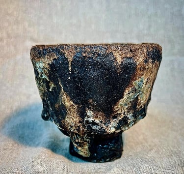 A handbuilt chawan cup for tea ceremony with black, brown and green stone matt texture