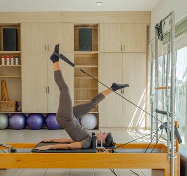 Woman lying on a Pilates Reformer doing a leg exercise using the foot straps in the Cabo San Lucas studio.