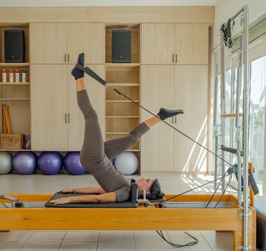 Woman lying on a Pilates Reformer doing a leg exercise using the foot straps in the Cabo San Lucas studio.