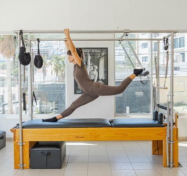 Woman doing a split stretch on a Pilates Cadillac apparatus in a bright studio in Cabo San Lucas.