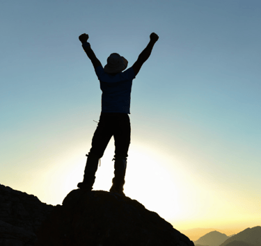 Silhouetted figure arms raised in success on peak